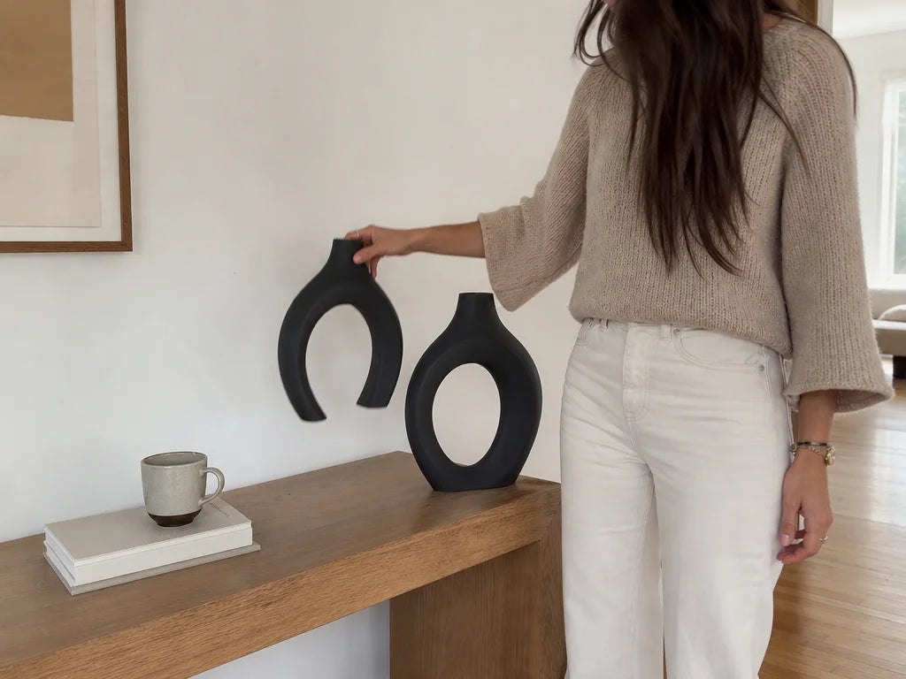 4:3 candid lived-with decor photograph. A woman in casual home clothes is casually lifting the hollo